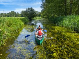 Two people paddling a canoe on a narrow river surrounded by trees and tall grass at Thorpe Forest Golden Oak Treehouse in Thorpe Forest