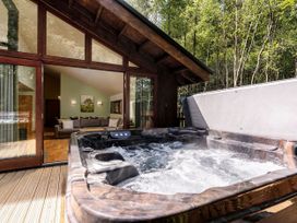 An outdoor hot tub on a wooden deck next to a cabin with large glass doors showing a sofa and dining area inside at Keldy Golden Oak in Keldy Forest