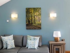 A grey sofa with patterned cushions a wooden side table with a lamp and a forest picture on a blue wall at Glentress Forest Silver Birch in Glentress Forest Peebles