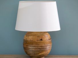 A table lamp with a wooden base and a white lampshade on a wooden surface against a blue wall at Glentress Forest Silver Birch in Glentress Forest Peebles