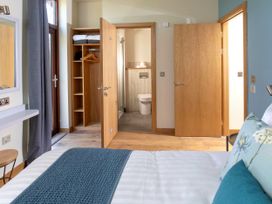 A bedroom with a bed blue and floral pillows a wardrobe with hangers and towels an open door to a bathroom and a wooden door at Glentress Forest Silver Birch Glentress Forest Peebles