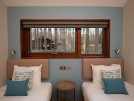 A bedroom with two single beds a round wooden side table and a window showing trees and a cabin outside at Glentress Forest Silver Birch Glentress Forest Peebles