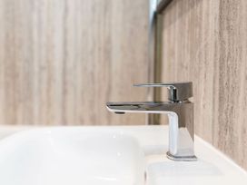 A close-up of a chrome faucet on a white sink with a textured wall in the background at Glentress Forest Silver Birch Glentress Forest Peebles