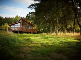 A wooden cabin with large glass windows and a deck surrounded by grass and trees at Cropton Silver Birch wheelchair accessible cabin in Cropton Forest