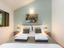 A bedroom with a double bed two bedside tables and a window with green curtains at Glentress Forest Golden Oak Treehouse Glentress Forest Peebles