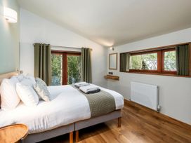 A bedroom with a bed and pillows next to two windows with green curtains at Glentress Forest Golden Oak Treehouse in Glentress Forest Peebles