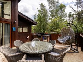 An outdoor deck with a round glass table surrounded by six wicker chairs a hanging wicker chair and a barbecue grill at Keldy White Willow Premium in Keldy Forest