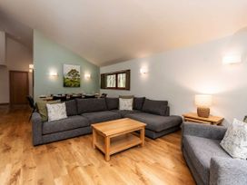 A living room with gray sofas a wooden coffee table and a dining table against a green wall at Strathyre Golden Oak Treehouse in Strathyre Ben Ledi