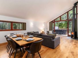 An open living and dining area with a wooden dining table set for eight and gray sofas near large windows and a wood stove at Strathyre Golden Oak Treehouse Strathyre Ben Ledi