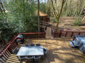 An outdoor wooden deck with dining table and chairs a hot tub and a barbecue grill in a forest setting at Strathyre Golden Oak Treehouse in Strathyre Ben Ledi
