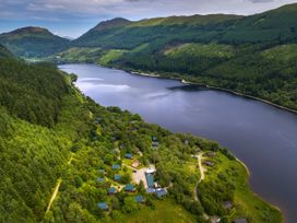 A lake surrounded by hills and dense forest with small houses along the shoreline at Strathyre Golden Oak Treehouse in Strathyre Ben Ledi
