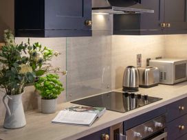 A kitchen countertop with a vase of flowers a plant an open cookbook a stovetop a kettle a toaster and a microwave at Keldy Golden Oak Hideaway in Keldy Forest