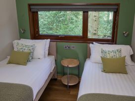 A bedroom with two single beds a small round wooden table between the beds and a window overlooking trees at Delamere Forest Golden Oak in Delamere Forest