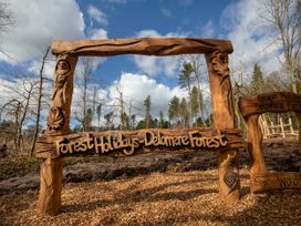 A wooden sign carved with Forest Holidays Delamere Forest in a forest area with trees and wood chips on the ground at Delamere Forest Silver Birch Delamere Forest