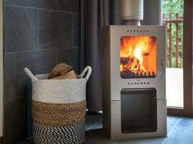 A wood burning stove with fire inside and a basket with firewood next to it at Strathyre White Willow Premium in Strathyre Ben Ledi