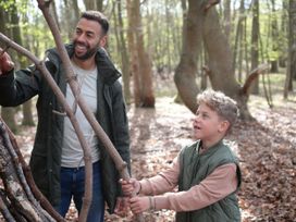 A man and a boy holding sticks in a forest with trees and fallen leaves at Strathyre White Willow Premium in Strathyre Ben Ledi