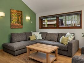 A living room with a gray sectional sofa with patterned pillows a wooden coffee table and a green accent wall with a forest painting at Thorpe Forest Golden Oak Thorpe Forest
