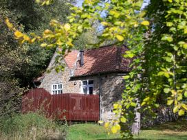 A stone cottage with a red tiled roof and wooden fence surrounded by trees and greenery at Keldy Golden Oak Cottage in Keldy Forest