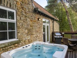 An outdoor patio with a hot tub a barbecue grill and a round table with chairs next to a stone building at Keldy Golden Oak Cottage Keldy Forest