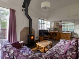 A living room with purple floral sofas a wood stove and a wooden coffee table next to a kitchen with a wooden counter at Keldy Golden Oak Cottage in Keldy Forest