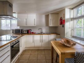 A kitchen with white cabinets wooden countertops a stove oven microwave toaster kettle dining table with wooden bowl and two chairs at Keldy Golden Oak Cottage in Keldy Forest