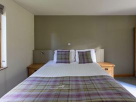 A bedroom with a double bed with plaid pillows and throw and wooden bedside tables at Keldy Golden Oak Cottage in Keldy Forest