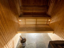 A wooden sauna room with two bench seats a metal bucket with a ladle and a heater with stones at Keldy Golden Oak Cottage in Keldy Forest
