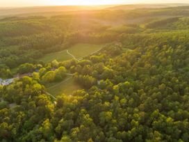 An aerial view of a forest with scattered houses and winding roads with the sun setting in the background at Keldy Golden Oak Cottage Keldy Forest
