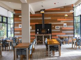 An indoor dining area with wooden tables and patterned chairs a stone fireplace on a wooden paneled wall at Keldy Golden Oak Cottage Keldy Forest