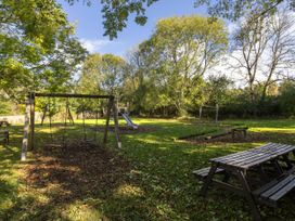 An outdoor playground with swings slide and picnic benches surrounded by trees at Keldy Golden Oak Cottage in Keldy Forest