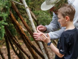 A man and a boy building a structure with wooden sticks in a forest at Keldy Golden Oak Cottage in Keldy Forest