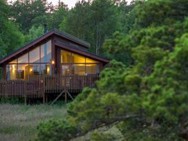 A wooden cabin with large windows and a deck surrounded by trees at Cropton Golden Oak in Cropton Forest