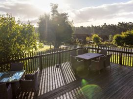 An outdoor wooden deck with two tables and wicker chairs surrounded by trees at Cropton Golden Oak in Cropton Forest