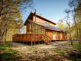 A wooden cabin with large windows and a wooden fence surrounded by trees at Strathyre Golden Oak in Strathyre Ben Ledi