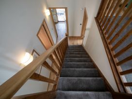 A staircase with a wooden railing and grey carpet leading to a hallway with wooden floors at Strathyre Golden Oak in Strathyre Ben Ledi