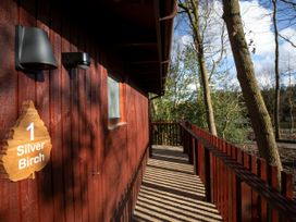 A wooden cabin entrance with a sign reading 1 Silver Birch and a porch railing amidst trees at Thorpe Forest Silver Birch wheelchair accessible cabin Thorpe Forest