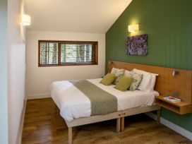 A bedroom with a double bed green accent wall and window with wooden blinds at Forest of Dean Meadow - Golden Oak in Forest Of Dean