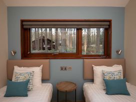 A bedroom with two single beds with pillows a small round wooden table and a window showing a forest view at Glentress Forest Silver Birch Glentress Forest Peebles