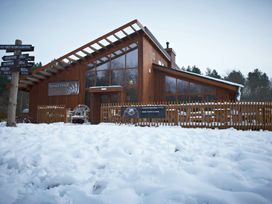 A wooden building with large windows and a fenced patio area surrounded by snow at Glentress Forest Silver Birch in Glentress Forest Peebles
