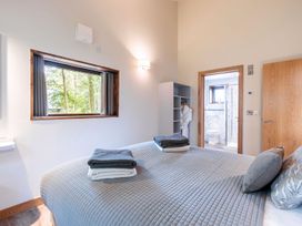 A bedroom with a bed towels on it a window a door leading to a bathroom and a shelving unit at Glentress Forest White Willow Premium in Glentress Forest Peebles