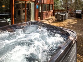 A deck with a hot tub dining table with chairs and a barbecue grill at Glentress Forest Golden Oak in Glentress Forest Peebles