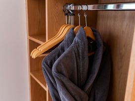 A wooden wardrobe with empty hangers and two gray bathrobes hanging inside at Glentress Forest Golden Oak Glentress Forest Peebles