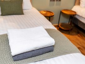 Folded white and gray towels on a bed with green cushion and wooden side tables in a bedroom at Glentress Forest Golden Oak Glentress Forest Peebles