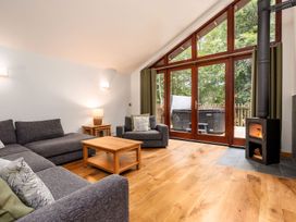 A living room with grey sofas a wooden coffee table a wood burning stove and large glass doors opening to a deck at Glentress Forest Golden Oak in Glentress Forest Peebles