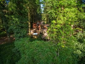 A wooden cabin with a deck and hot tub surrounded by dense trees at Glentress Forest Golden Oak Treehouse Glentress Forest Peebles