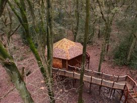 A hexagonal wooden treehouse with a shingled roof and a rope bridge entrance in a leafless forest Glentress Forest Golden Oak Treehouse Glentress Forest Peebles