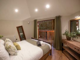 A bedroom with a bed two rolled towels a wooden dresser with a plant and a balcony with green curtains at Glentress Forest Golden Oak Treehouse in Glentress Forest Peebles