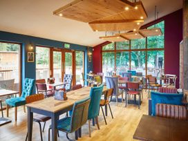 A dining area with wooden tables and mixed chairs and large windows showing trees at Thorpe Forest Silver Birch in Thorpe Forest