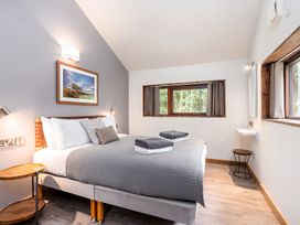 A bedroom with a double bed grey bedding two windows and wooden floor at Glentress Forest White Willow Premium Glentress Forest Peebles