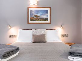 A bed with white and patterned pillows a grey quilt and folded towels on each side with reading lamps and a framed landscape photo above at Glentress Forest White Willow Premium in Glentress Forest Peebles